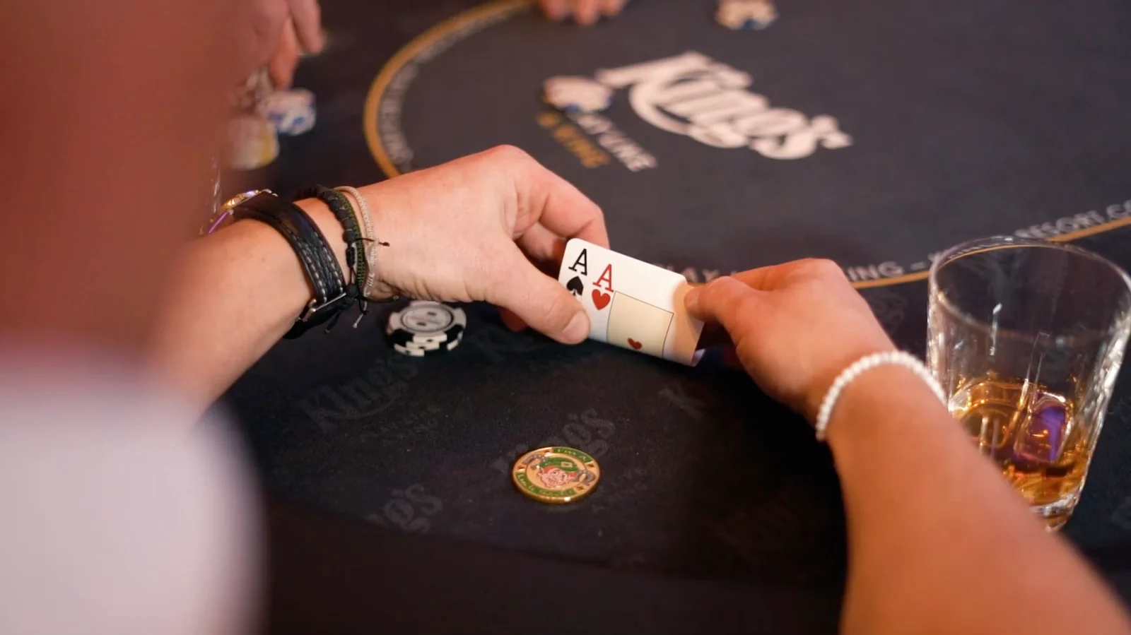 Ein Spieler hebt am Tisch im King's Casino Rozvadov seine beiden Karten an, zwei Asse, daneben liegen Chips und ein Glas.