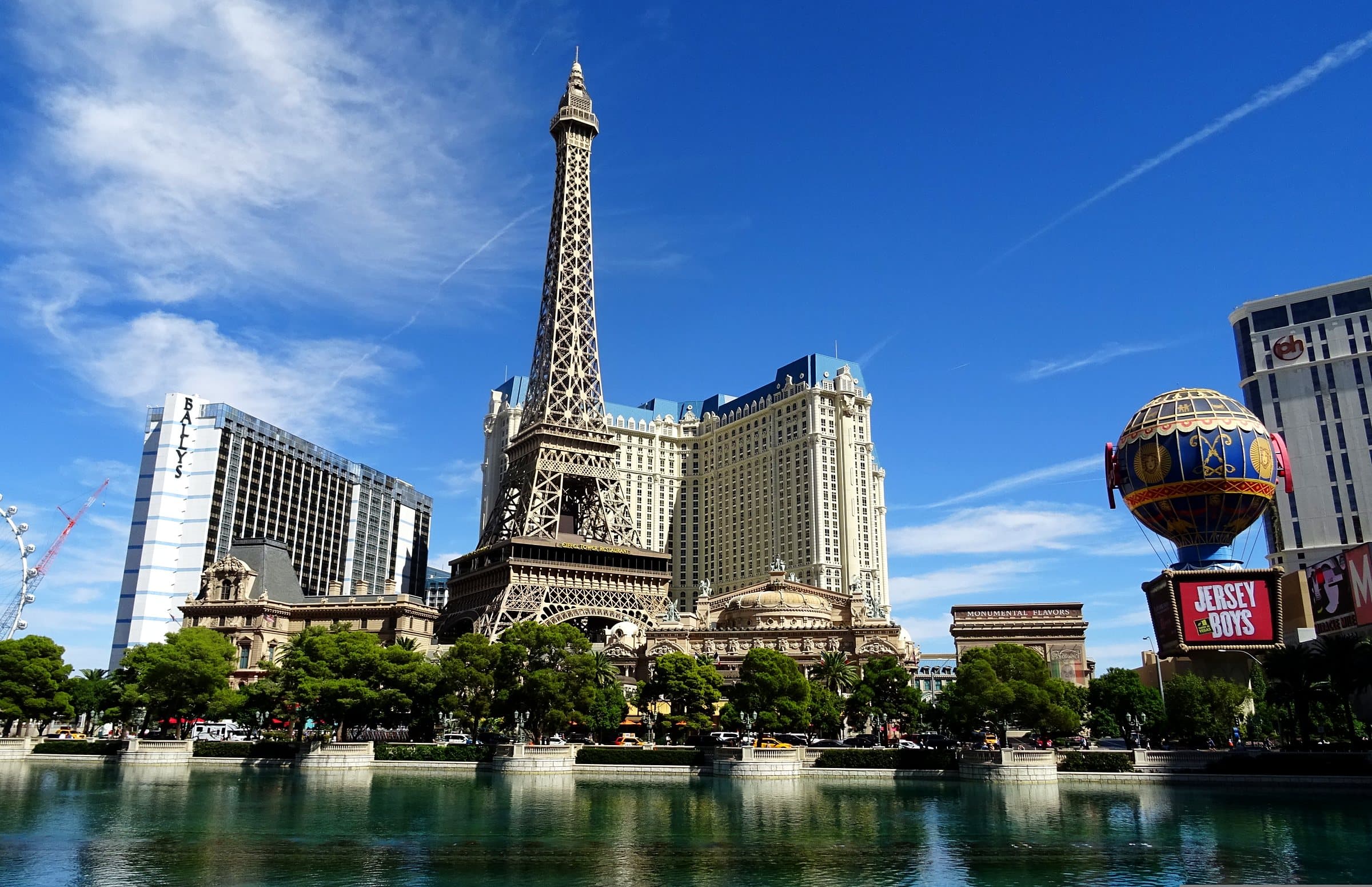 Der Las Vegas Strip bei Tag unter blauem Himmel, mit dem Eiffelturm-Nachbau und dem Ballon des Paris Las Vegas, dem Bally's und dem See des Bellagio im Vordergrund.