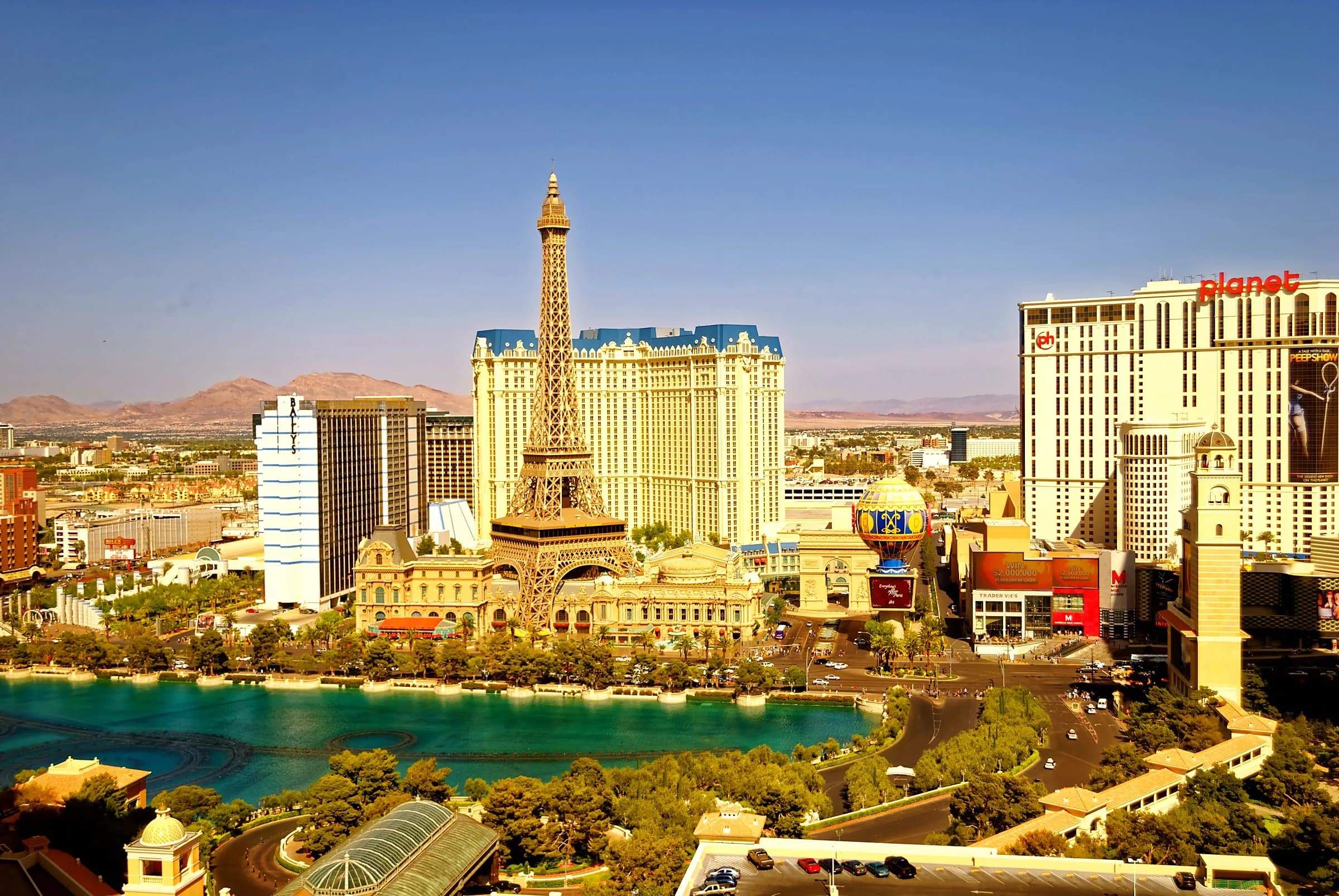 Der Las Vegas Strip bei Tag unter blauem Himmel, mit dem Eiffelturm-Nachbau und dem Ballon des Paris Las Vegas, dem Bally's und dem See des Bellagio im Vordergrund.